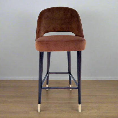 Brown bar stool with black metal legs on a wooden floor.