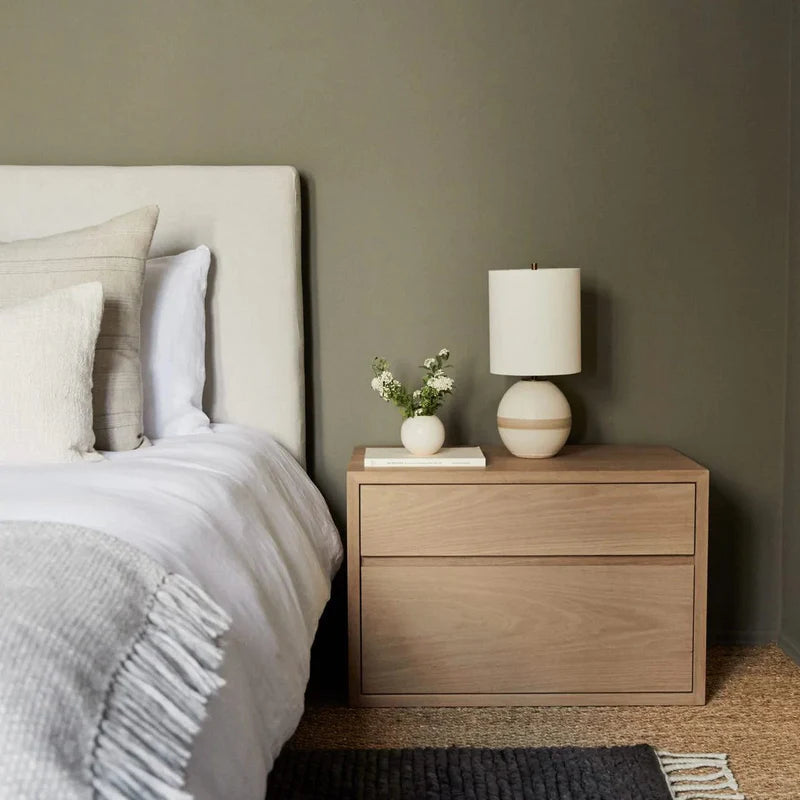 Bedroom with a wooden nightstand, lamp, and decorative items against a gray wall.
