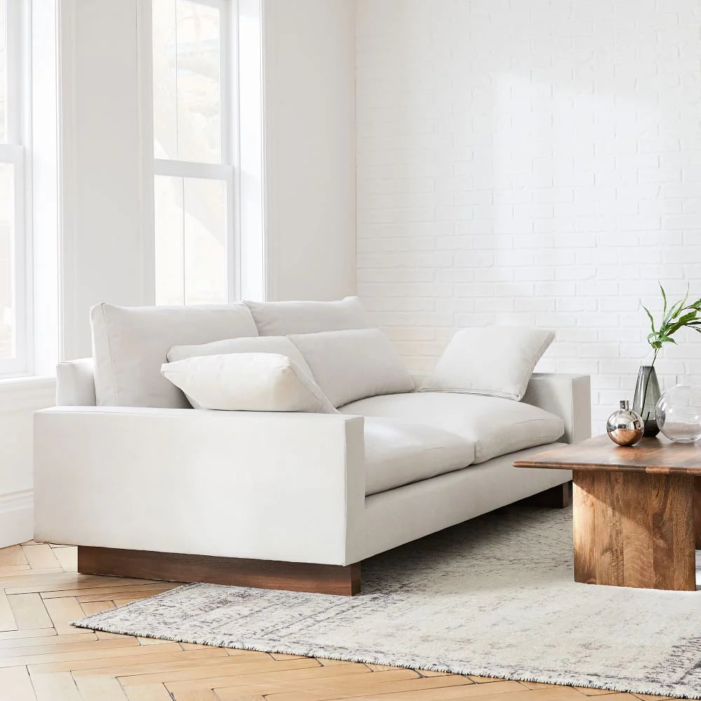 White sofa in a modern living room with wooden coffee table and large windows.