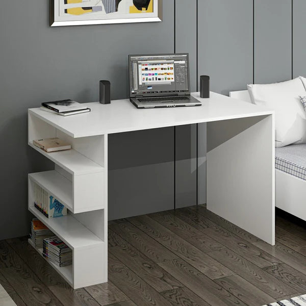 White L-shaped desk with a laptop, speakers, and books in a room with a gray wall and wooden floor.