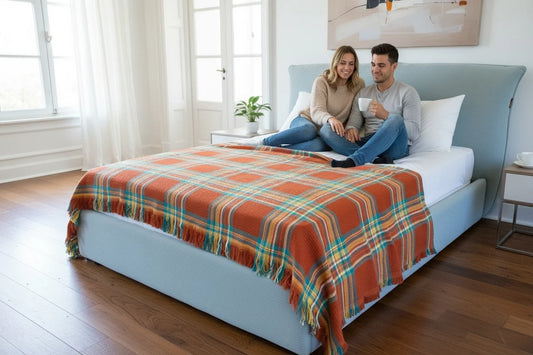 Couple sitting on a bed with a plaid blanket in a bright bedroom.