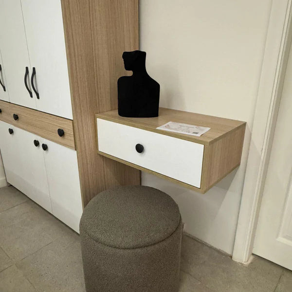 Small wooden desk with a white drawer, black vase, and gray stool in a room.