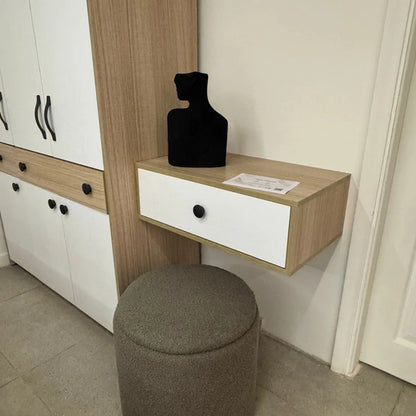 Small wooden desk with a white drawer, black vase, and gray stool in a room.