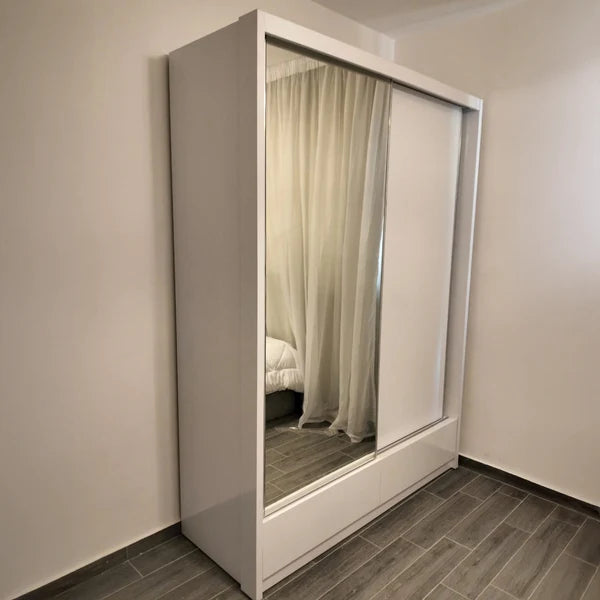 White wardrobe with a mirror in a room with beige walls and wooden flooring.