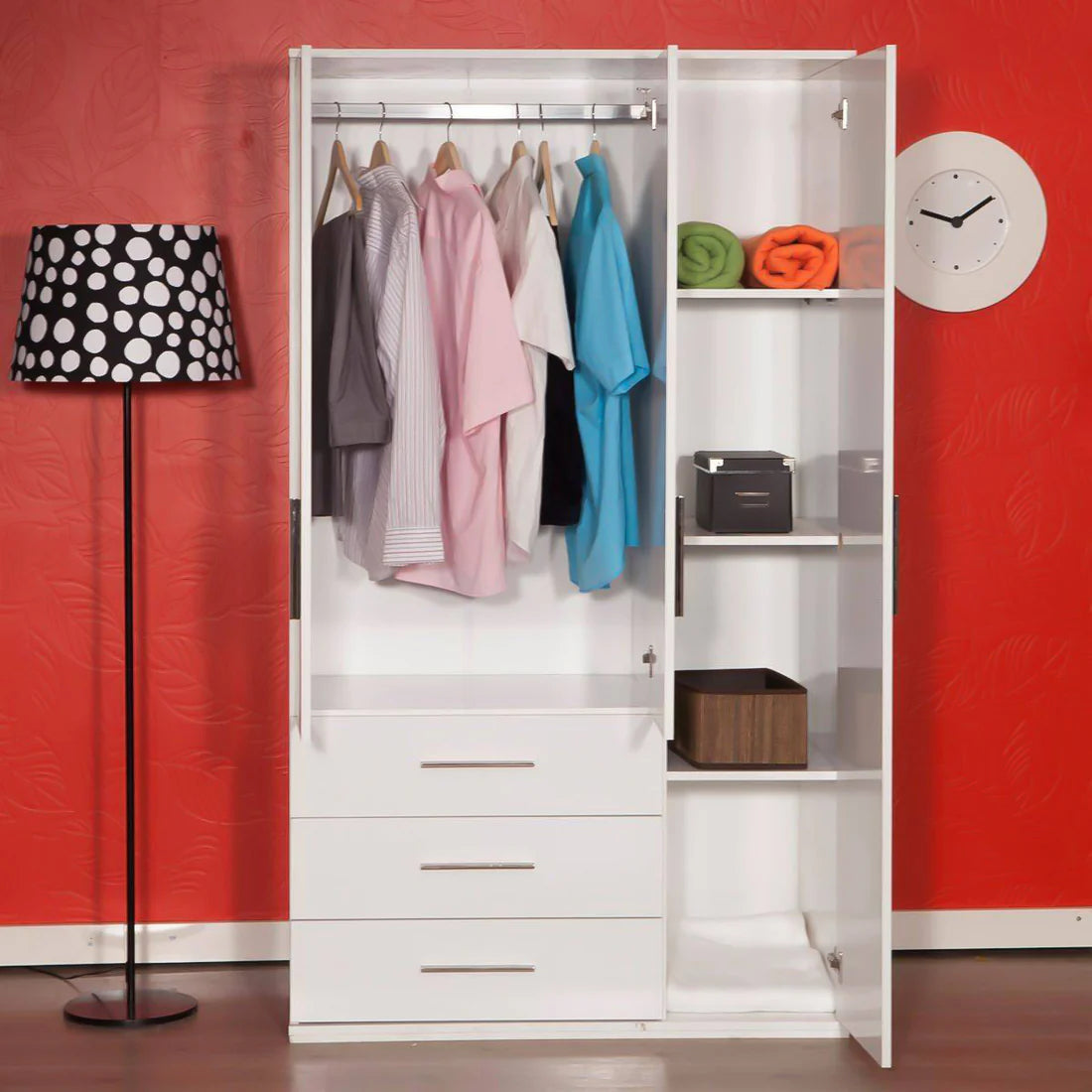 White wardrobe with clothes and shelves against a red wall with a lamp and clock.