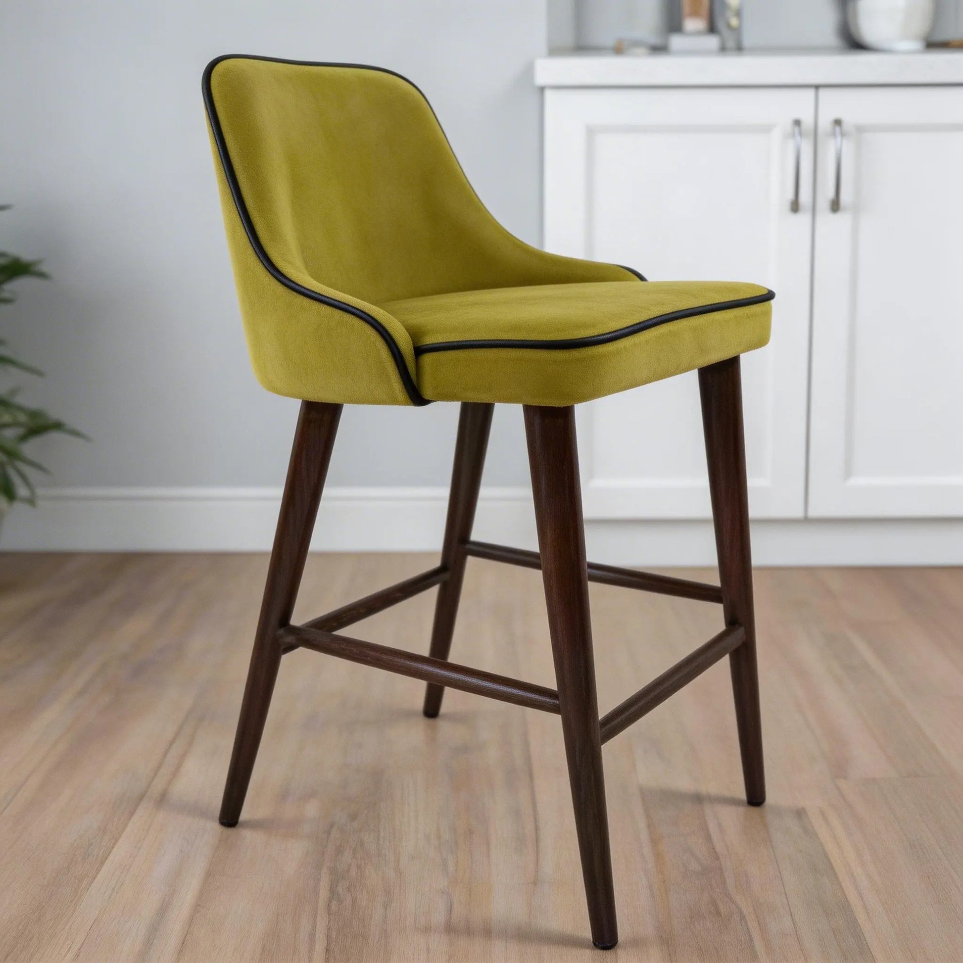Green bar stool with wooden legs in a room with white cabinets and a plant.