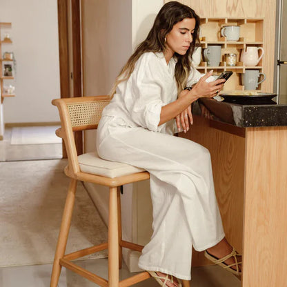 Woman in a white outfit sitting on a wooden chair in a kitchen, using a phone.